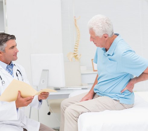 Patient sitzt auf der Liege beim Arzt und greift sich auf den Rücken