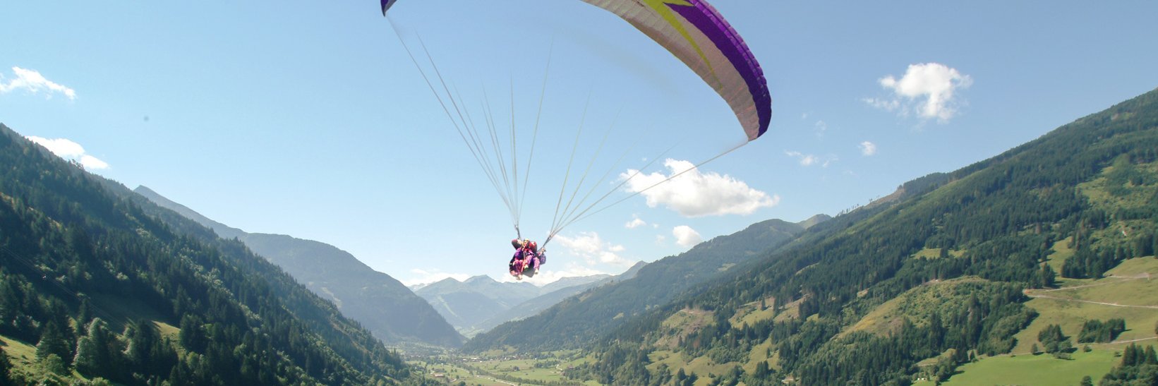 Paragleiter schwebt über Gastein, vor ihm ein Panorama aus grünen Almen, Wäldern und Bergen.