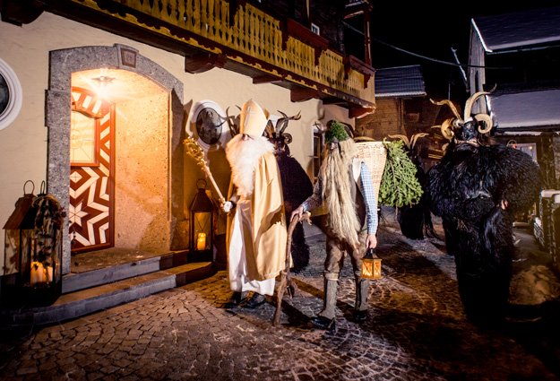 Krampus, Nikolaus und Körbelträger vor einem Haus