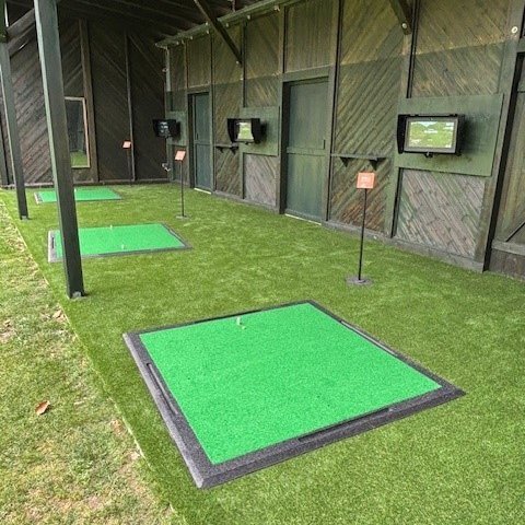 Der Golfbereich zeigt grüne Matten auf einem Kunstrasenboden, umgeben von Holzwänden und Bildschirmen.