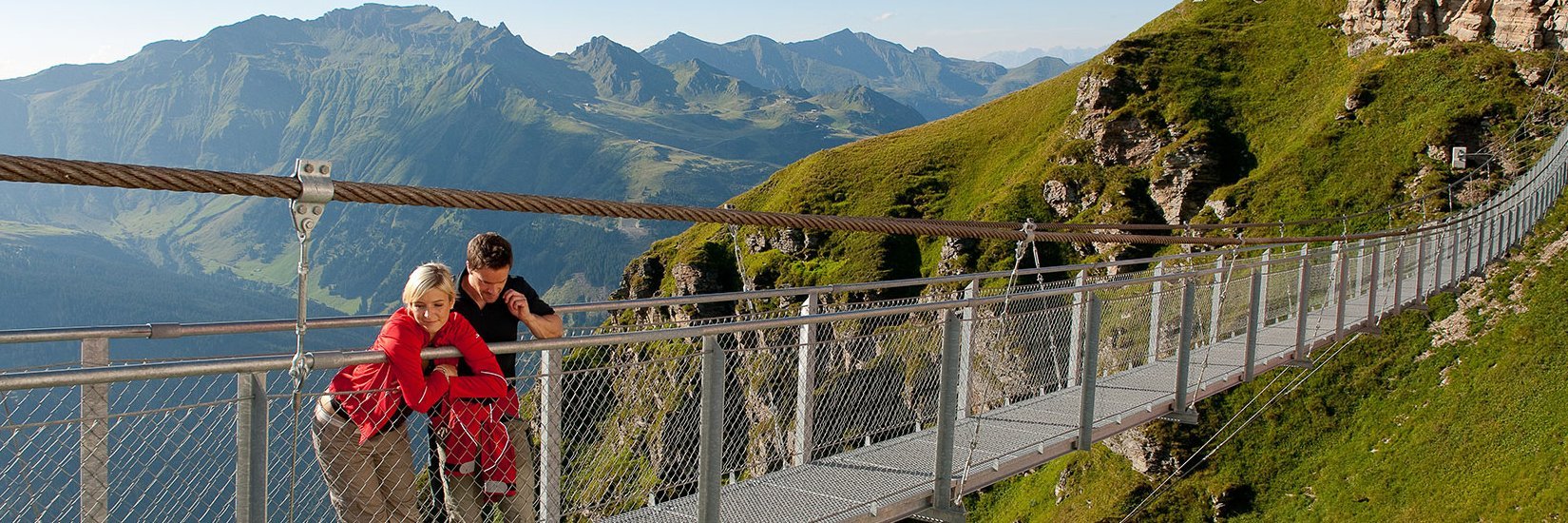 Zwei Besucher genießen die Aussicht von der Hängebrücke, es ist Sommer, die Wiesen sind grün und die Aussicht atemberaubend. Almorama in Gastein.