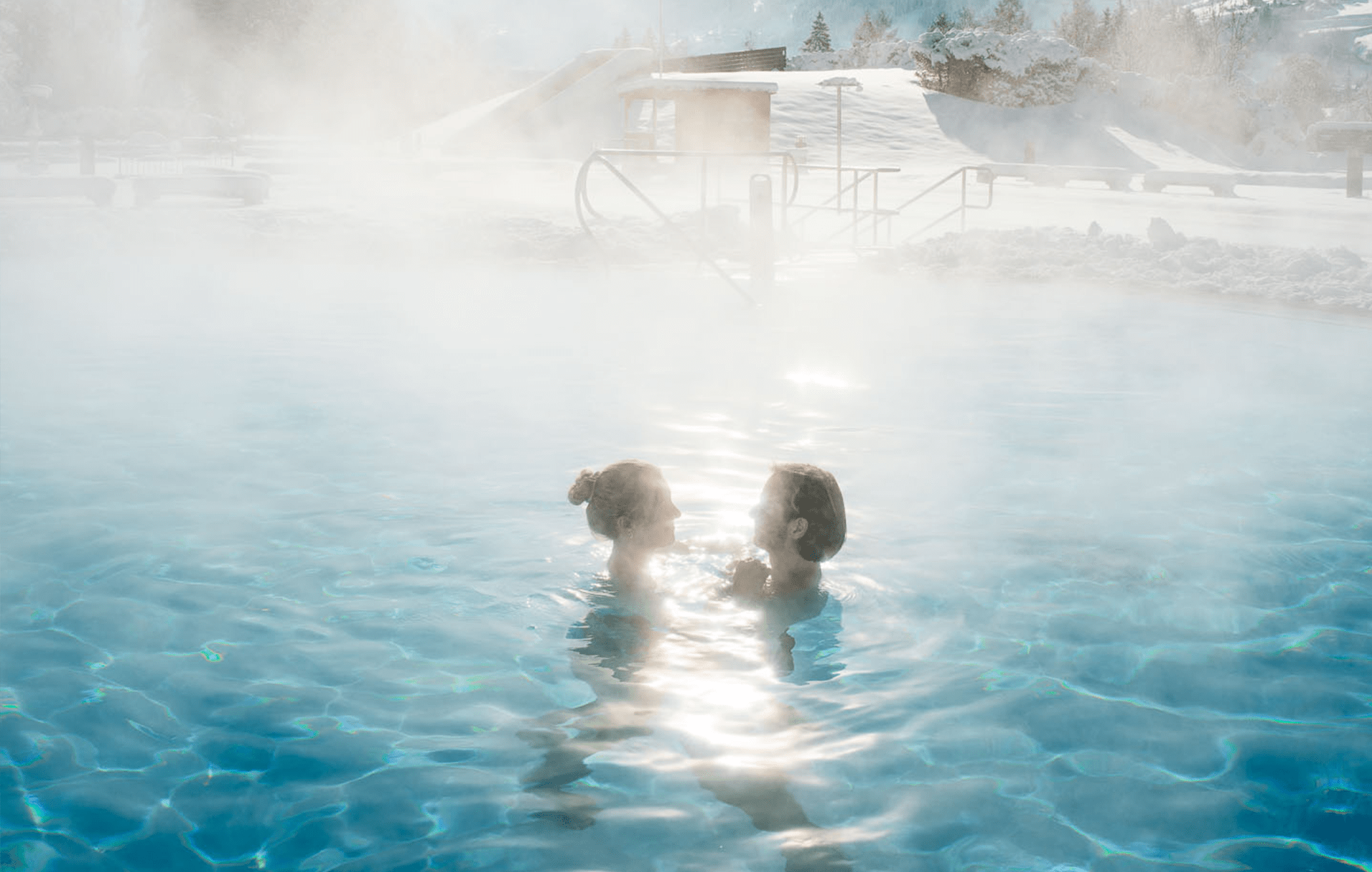 A couple in the warm outdoor thermal water pool with a snow-covered landscape in the background