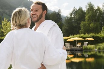 Fröhliches Paar in Bademänteln vor dem Naturbecken einer Therme in Gastein