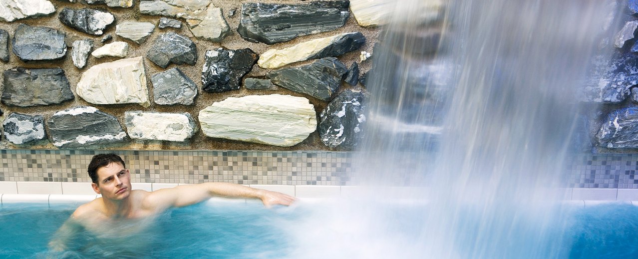 Mann im Thermalwasserbecken neben einem kleinen Wasserfall