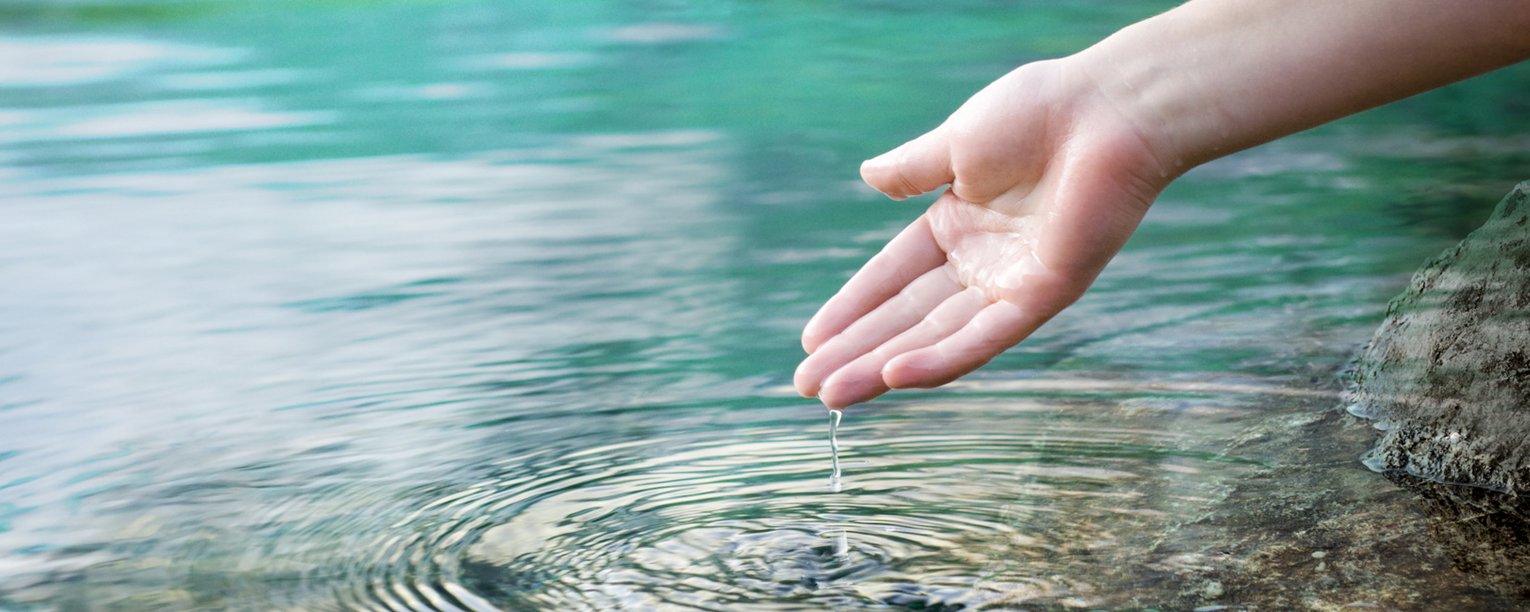 Hand einer Person vor der Wasseroberfläche eines Sees