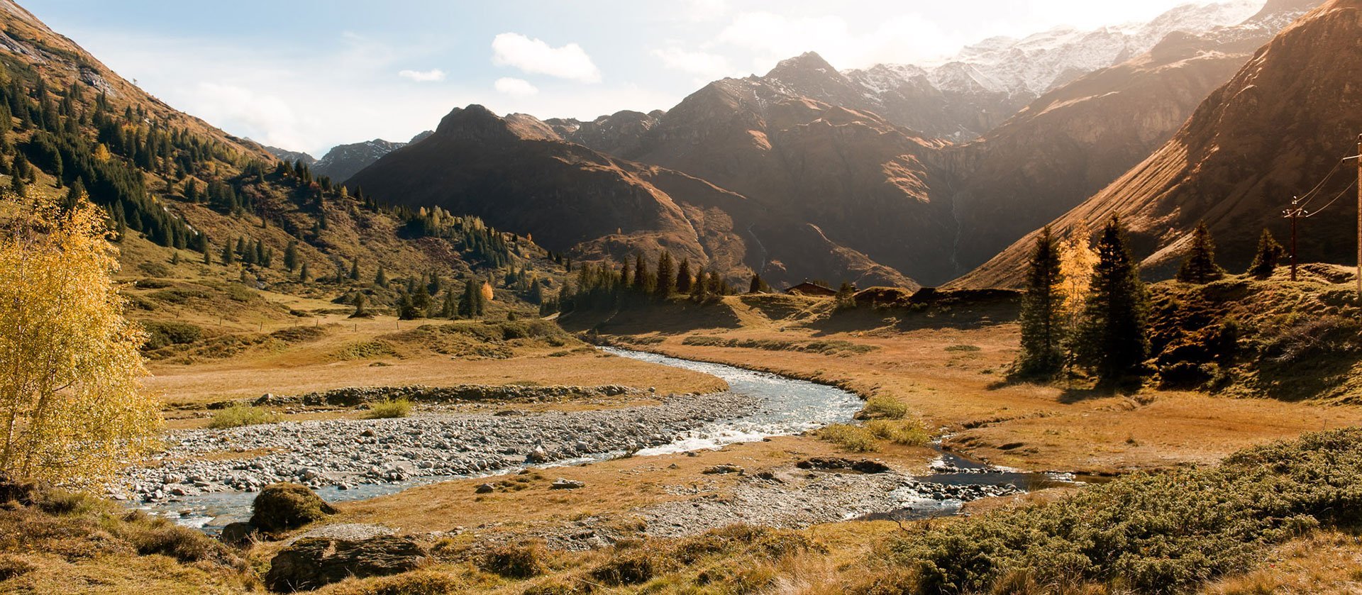 Herbstliche Berglandschaft im Gasteinertal mit alpinem Fluss im Vordergrund und warmem Sonnenlicht über den umliegenden Gipfeln.