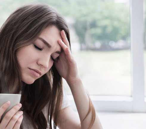 Frau mit Tasse in der Hand greift sich an die Stirn